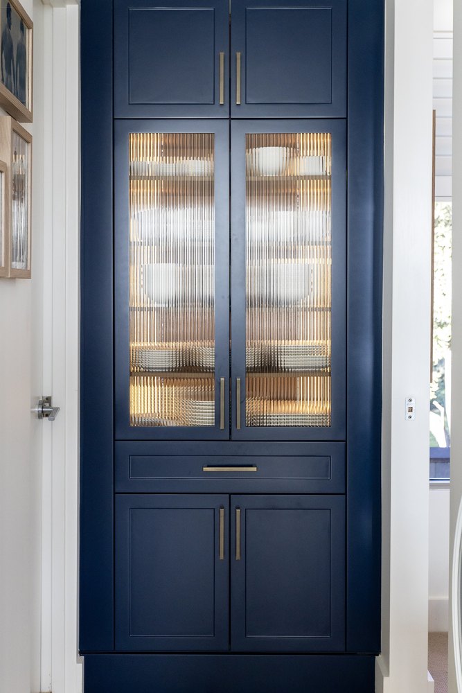 A tall navy cabinet with lit fluted-glass doors and brass handles